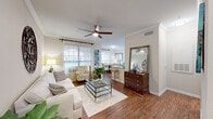 Located in Houston, TX, this well-appointed single-story residence offers one bedroom and two full bathrooms within a thoughtfully designed floor plan. The open-concept living and dining area is anchored by rich hardwood-style flooring, crown molding, and ceiling fans that enhance the bright, airy atmosphere. Large windows dressed with sheer curtains and blinds invite abundant natural light throughout. The dining area comfortably accommodates a full-sized table and benefits from direct access to an exterior door with a transom window above, further brightening the space. The galley-style kitchen features warm wood cabinetry, granite-style countertops, a stone tile backsplash, and black appliances including a refrigerator, range, microwave, and dishwasher. The bedroom is a comfortable retreat with plush carpet, a ceiling fan, and natural light from exterior-facing windows. A spacious walk-in closet with wire shelving provides generous storage. The primary bathroom includes a soaking tub with shower, granite vanity, and hardwood-style flooring. A dedicated laundry area houses a full-size washer and dryer. Crown molding and consistent finishes throughout tie the entire space together cohesively.