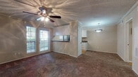 This single-floor residence offers a thoughtfully designed layout across one bedroom and one bathroom. The open living area features plush wall-to-wall carpeting, crown molding, and a ceiling fan with integrated lighting, creating a comfortable and inviting atmosphere. Large glass doors lead to a private outdoor balcony, allowing natural light to fill the space while providing outdoor views. A pass-through counter connects the living area to the kitchen, enhancing the open feel between the two spaces. The galley-style kitchen is well-equipped with white cabinetry, dark granite-style countertops, hardwood flooring, and a suite of black stainless appliances including a refrigerator, electric range, dishwasher, and a dedicated window that brings in additional natural light. The spacious bedroom continues the carpeted flooring and crown molding found throughout, with its own ceiling fan and a window overlooking the outdoors. The bathroom features hardwood flooring, a full tub-shower combination with classic white tile surround, and a generous vanity with dark stone-style countertops and white cabinetry, completing this functional and comfortable home.
