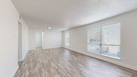 This single-story unit offers a clean, modern aesthetic throughout its well-organized layout. The open living area is a standout feature, characterized by light wood-style plank flooring, crisp white walls, and a textured ceiling. Multiple windows fitted with horizontal blinds allow natural light to fill the space, creating a bright and welcoming atmosphere.

The galley-style kitchen is efficiently designed with white shaker cabinetry accented by matte black hardware, light speckled countertops, a stainless steel double-basin sink with a black pull-down faucet, and an electric range. A window at the end of the kitchen provides additional natural light. The layout also includes a dedicated nook area suitable for use as a dining space or utility zone.

Both bedrooms feature neutral carpet flooring, ceiling fans with integrated lighting, and windows with blinds. One bedroom includes a built-in closet with bi-fold doors. A dedicated storage or laundry nook with wood-style flooring is also present within the unit.

The bathroom is finished in a consistent white palette, featuring a vanity with speckled countertop, a framed mirror, matte black fixtures, and a tub-shower combination with tiled surround. The cohesive use of black accents and neutral tones throughout gives the unit a modern, coordinated feel.