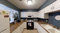 Located at 11415 Knollridge Ln in Indianapolis, Indiana, this single-story home offers a comfortable and functional layout designed for everyday living. The kitchen is a standout feature of the home, showcasing a clean and classic aesthetic with crisp white cabinetry that lines the walls from counter to ceiling, providing generous storage throughout. Rich, dark-toned countertops offer a striking contrast against the white cabinets and the bold navy blue walls, creating a visually dynamic and welcoming space. The kitchen is equipped with a gas range, over-the-range microwave, and a double-basin sink, making it both practical and well-suited for home cooking. Light tile flooring runs underfoot, adding a bright, easy-to-maintain surface to the space. A textured ceiling and flush-mount light fixture complete the room's classic character. The navy blue wall color carries a strong, cohesive design statement throughout the kitchen, lending the space a sense of personality and warmth. Natural light filters in through a nearby window, further brightening the interior. Overall, this single-floor home presents a functional and characterful living environment in a residential Indianapolis neighborhood.