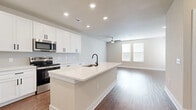 This single-floor residence offers a thoughtfully designed layout encompassing a living room, kitchen, bedroom, bathroom, and closet. The open-concept kitchen serves as the heart of the home, featuring crisp white shaker cabinetry with matte black hardware, gleaming quartz countertops, a herringbone tile backsplash, and a large center island with an undermount sink. Stainless steel appliances, including a refrigerator, range, and built-in microwave, complete the kitchen's modern aesthetic. Warm hardwood-style flooring flows throughout the main living areas, complemented by recessed lighting and a ceiling fan that enhance both style and comfort. The living room is bright and open, with natural light streaming in through slatted blinds. The bedroom is a serene retreat finished with plush carpet, a ceiling fan, and large windows that allow ample natural light to fill the space. A dedicated closet provides convenient storage. The bathroom is well-appointed with a tiled soaking tub and shower combination, a white vanity with quartz countertop, and matching matte black fixtures and hardware. Neutral warm tones and clean lines throughout create a cohesive, modern ambiance.