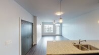This single-floor residence presents a thoughtfully designed open-concept layout that seamlessly connects the living, dining, and kitchen areas. Dark hardwood-style flooring runs throughout the main living spaces, complementing the neutral, light-toned walls that lend a clean and contemporary feel to the interior.

The kitchen is a standout feature, equipped with rich dark cabinetry extending to the ceiling for ample storage, granite countertops, a white subway tile backsplash, and a full suite of stainless steel appliances including a range, microwave, and refrigerator. A peninsula with a built-in sink and matching granite surface provides additional workspace and serves as a natural divider between the kitchen and living area.

The living area benefits from natural light delivered through large windows overlooking the surrounding building exterior, and a ceiling fan adds both comfort and function. A set of dark double doors provides a striking entryway accent. The bedroom features plush carpeting, a ceiling fan, and a window with an exterior view. The bathroom is finished with a dark vanity, granite countertop, and a tub-shower combination, maintaining the cohesive design aesthetic found throughout the space.