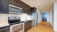 Located at 300 Alexander Ct in Philadelphia, PA, this efficiently designed studio offers a clean, modern aesthetic across a single level. The open living area is bathed in natural light streaming through a bank of three large windows dressed with white blinds, framing sweeping views of the Philadelphia skyline and surrounding cityscape. Light-toned hardwood flooring runs throughout, complementing the neutral gray walls and crisp white trim for a contemporary, cohesive look.

The galley-style kitchen is outfitted with rich, dark espresso cabinetry paired with stainless steel appliances, including a range, over-the-range microwave, dishwasher, and refrigerator. A classic white subway tile backsplash and light countertops provide a striking contrast to the dark cabinetry, adding a polished finish to the space.

The full bathroom features a soaking tub and shower combination with white tile surround, a dark-stained vanity with a clean countertop, and tile flooring, maintaining the modern design language found throughout. A dedicated closet provides well-organized storage with built-in shelving and hanging rods. Recessed lighting and thoughtful layout details complete this functional and stylish urban residence.