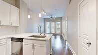 This thoughtfully designed one-bedroom, one-bathroom unit offers an efficient and functional single-floor layout with modern finishes throughout. The open-concept kitchen and living area serves as the heart of the space, featuring rich hardwood-style flooring, crisp white cabinetry, stainless steel appliances including a range, microwave, refrigerator, and dishwasher, and a decorative tile backsplash. A kitchen island with a stainless steel sink and pendant lighting adds both practicality and style. The living area extends toward a set of full-length French doors flanked by large windows, allowing abundant natural light and providing outdoor views. A ceiling fan adds comfort to this open gathering space. The bedroom is carpeted for warmth and comfort, featuring windows that bring in additional natural light and views of the surrounding area. Two closets provide generous storage options throughout the unit. The bathroom is finished with tile flooring, a white vanity with a framed mirror, and a tub-shower combination. Additional conveniences include a dedicated laundry area. Neutral wall tones and clean architectural lines give the entire space a bright, contemporary feel that is both inviting and easy to personalize.