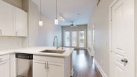 This thoughtfully designed one-bedroom, one-bathroom unit offers an efficient and functional single-floor layout with modern finishes throughout. The open-concept kitchen and living area serves as the heart of the space, featuring rich hardwood-style flooring, crisp white cabinetry, stainless steel appliances including a range, microwave, refrigerator, and dishwasher, and a decorative tile backsplash. A kitchen island with a stainless steel sink and pendant lighting adds both practicality and style. The living area extends toward a set of full-length French doors flanked by large windows, allowing abundant natural light and providing outdoor views. A ceiling fan adds comfort to this open gathering space. The bedroom is carpeted for warmth and comfort, featuring windows that bring in additional natural light and views of the surrounding area. Two closets provide generous storage options throughout the unit. The bathroom is finished with tile flooring, a white vanity with a framed mirror, and a tub-shower combination. Additional conveniences include a dedicated laundry area. Neutral wall tones and clean architectural lines give the entire space a bright, contemporary feel that is both inviting and easy to personalize.