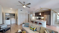 This single-story, 2-bedroom, 2-bathroom unit offers a thoughtfully designed open-concept layout that seamlessly connects the living, dining, and kitchen areas. Light wood-tone flooring flows throughout the main living space, complemented by neutral wall tones and ceiling fans in each room.

The kitchen is a standout feature, showcasing dark wood cabinetry extending to the ceiling, granite-style countertops, a white subway tile backsplash, and a full suite of stainless steel appliances including a range, microwave, and refrigerator. A central island with seating provides additional prep space and a casual dining option. The adjacent dining area benefits from large windows dressed with patterned curtains, allowing ample natural light.

The living area is generously proportioned, with windows offering natural light and an in-unit washer visible nearby. Both bedrooms are well-sized, each featuring a ceiling fan, carpeted flooring, and windows with blinds.

The two bathrooms are finished with granite-topped vanities and dark cabinetry. The primary bathroom includes a glass-enclosed walk-in shower with white tile surround, while the secondary bathroom offers a full soaking tub with a tiled surround.