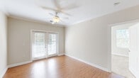 Located at Fairway Village in Whitsett, NC, this well-appointed 2-bedroom, 2-bathroom single-floor residence offers a thoughtfully designed layout with a comfortable, functional flow throughout. The open-concept living, dining, and kitchen area serves as the heart of the home, featuring warm hardwood-style flooring, crown molding, and a ceiling fan. French doors flood the living room with natural light and open to a private balcony. The kitchen is equipped with rich dark cabinetry, granite countertops, a center island with a sink, and a full suite of stainless steel appliances, including a range, microwave, and refrigerator. A pantry provides additional storage convenience. Both bedrooms are carpeted and fitted with ceiling fans and ample natural light from large windows. The spacious primary bedroom includes an expansive walk-in closet with wire shelving on both sides. The bathrooms feature tile flooring and dark wood vanities with brushed nickel hardware. A dedicated in-unit laundry room with washer and dryer hookups, multiple closets throughout, and a utility room round out the practical amenities of this well-designed residence.