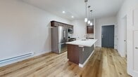 This 480 square foot apartment in Fitchburg, Wisconsin, offers a thoughtful blend of modern design and efficient space utilization. The single-floor layout comprises one bedroom, one bathroom, a kitchen, and a closet, creating a cozy yet functional living space.

The heart of the apartment is the open-concept kitchen, which showcases contemporary dark wood cabinetry and stainless steel appliances. A large central island with a white countertop serves as both a food preparation area and a casual dining space. Pendant lighting adds a touch of elegance, while the light wood flooring throughout creates a warm, inviting atmosphere.

The bathroom features a clean, minimalist design with a spacious vanity, large mirror, and a combined shower-bathtub unit. White tiles and fixtures contribute to a bright, airy feel. The bedroom, measuring 110 square feet, is carpeted for comfort and includes a large window that allows natural light to flood the space.

Climate control is ensured through a wall-mounted air conditioning unit, and a ceiling fan in the main living area aids in air circulation. The apartment's neutral color palette, predominantly whites and light grays, creates a sense of spaciousness and allows for personalization.

Despite its compact size, this apartment maximizes every square foot, offering a comfortable and stylish living environment for singles or couples seeking a modern urban lifestyle.