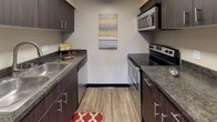 Located at 3501 Stover St in Fort Collins, Colorado, this single-floor residence offers a thoughtfully designed layout with a warm, contemporary aesthetic throughout. The living room is a welcoming focal point, featuring neutral-toned walls accented by a bold charcoal feature wall, plush carpeting, and a bank of windows with blinds that invite abundant natural light and outdoor views. The kitchen is efficiently arranged with dark espresso cabinetry, granite-style countertops, wood-look flooring, and stainless steel appliances including a range, microwave, and ample counter workspace. Adjacent to the kitchen, the dining area accommodates a full-sized table beneath a classic chandelier, with rich hardwood-style flooring that completes the space. The primary bedroom is generously sized, carpeted, and features multiple windows for natural light, while a secondary bedroom offers flexible use as a study or home office with built-in shelving and a work desk. A third bedroom includes a bunk bed setup with a closet, ideal for versatile sleeping arrangements. The bathroom is clean and functional, offering a soaking tub and shower combination, dark wood vanity with granite-style countertop, and wood-look flooring, providing a relaxing retreat.
