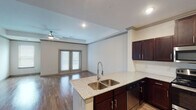 This single-story residence in Magnolia, Texas offers a thoughtfully designed open-concept layout that maximizes both functionality and comfort. The living area is anchored by rich wood-style hardwood flooring that reflects natural light streaming in through multiple windows and a set of double glass doors, which also provide access to the outdoors. A ceiling fan overhead adds to the airy, comfortable atmosphere of the space.

The kitchen is a standout feature, equipped with a full suite of stainless steel appliances including a range, microwave, and French door refrigerator. Dark espresso cabinetry provides ample storage and contrasts beautifully with the light granite countertops. A kitchen island with a double stainless steel sink and additional seating space connects seamlessly to the living area, making it ideal for both cooking and entertaining.

The bedroom is a peaceful retreat, finished with plush wall-to-wall carpet, a ceiling fan, and two generous windows that allow natural light to fill the room. The bathroom continues the refined aesthetic with granite countertops, dark cabinetry, wood-style flooring, and a separate water closet with a stall shower. The unit also includes a dedicated entryway with a closet, completing this well-rounded and move-in-ready home.