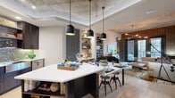 This single-floor urban residence masterfully combines industrial character with contemporary design. Exposed concrete ceilings and a dramatic brick accent wall establish a loft-inspired aesthetic throughout the living areas, while light wood flooring and crisp white walls provide a clean, modern contrast.

The open-concept kitchen is a standout feature, equipped with rich dark wood cabinetry, stainless steel appliances, a striking mosaic tile backsplash, a farmhouse-style sink, and a large island with a white quartz countertop and integrated open shelving. A trio of black pendant lights illuminates the island, which extends seamlessly into the dining area.

The living room offers a welcoming, well-lit retreat anchored by a sectional sofa and a sputnik-style pendant light. French doors open directly onto a private balcony, flooding the space with natural light and providing outdoor views. A sliding barn door adds a functional architectural accent.

The primary bedroom benefits from large windows with exterior views, an exposed concrete ceiling, and direct access to a well-appointed en-suite bathroom. The bathroom features a glass-enclosed walk-in shower with subway tile walls, a mosaic tile floor, dark cabinetry, and a wide vanity with ample counter space. A secondary bedroom offers a comfortable, cozy retreat with its own en-suite access.