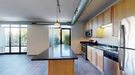 Located at 2401 Chicago Ave in Minneapolis, MN, this one-bedroom, one-bathroom unit offers a well-designed layout with industrial-modern character. The combined kitchen and living area serves as the heart of the space, featuring exposed metallic ductwork that adds an urban loft aesthetic. Floor-to-ceiling windows flood the room with natural light and frame lush outdoor greenery, creating a bright and inviting atmosphere. The kitchen is equipped with stainless steel appliances, including a gas range, microwave, and refrigerator, complemented by dark granite countertops and light maple cabinetry. A central kitchen island with a matching granite surface provides additional prep space and a natural gathering point. Hardwood-style flooring runs throughout the main living areas, lending warmth and cohesion to the space. The bedroom is carpeted for comfort and features direct access to a walk-in closet with built-in shelving. The bathroom includes a full tub-shower combination with hardwood-style flooring that mirrors the main living areas. A dedicated laundry area houses a stacked washer and dryer unit, adding everyday convenience. Two closets provide ample storage throughout the unit, rounding out this efficiently designed and thoughtfully appointed space.