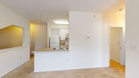 This single-floor, one-bedroom, one-bathroom residence offers a practical and efficiently designed layout. The open living area is carpeted and bathed in natural light from windows flanking the front entry door, creating a welcoming atmosphere upon arrival. The kitchen is designed in a galley style, featuring white cabinetry, a stainless steel double-basin sink, light wood-style flooring, and white appliances including a refrigerator, electric range, and built-in microwave. A pass-through counter with a built-in wine rack niche connects the kitchen to the living area, enhancing the open feel of the shared space. The bedroom is comfortably sized with plush carpet, a ceiling fan, and a corner window configuration that allows ample natural light and outdoor views. Adjacent to the bedroom is a generously sized walk-in closet, outfitted with wire shelving and multi-tiered storage racks for organized storage. The bathroom features tile flooring, a white vanity with cabinet storage, a large mirror, and a well-lit vanity light bar. Throughout the residence, neutral tones and clean white trim create a cohesive, light, and airy aesthetic.