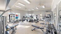 Located at 2000 Central Parkway in Montgomery, Alabama, this fitness center offers a thoughtfully designed exercise space that accommodates a wide variety of workout routines. The room features light gray walls accented by a bold blue feature wall, crown molding, and a neutral-toned carpet floor that lends a clean, polished aesthetic throughout.

Natural light pours in through multiple large windows, providing views of the surrounding outdoor amenity areas, including what appears to be a pool and landscaped grounds. Ceiling fans and recessed panel lighting ensure the space remains well-ventilated and brightly lit at all times.

The exercise room is comprehensively outfitted with an impressive array of equipment. Cardio offerings include treadmills, elliptical trainers, a stationary bike, and a rowing machine, while strength training is supported by cable machines, a multi-station weight system, free weights, a dumbbell rack, and multiple adjustable benches. Medicine balls and stability balls on a dedicated rack add further variety for functional fitness training. Large wall-mounted mirrors enhance the sense of space and allow users to monitor their form. A wall-mounted television provides entertainment during workouts.

A glass-panel door provides direct access to the outdoor area, seamlessly connecting the interior fitness space to the broader community amenities outside.