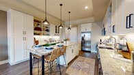 This thoughtfully designed single-floor residence offers a seamless blend of modern functionality and eclectic style. The open-concept kitchen is a standout centerpiece, featuring two-tone cabinetry with crisp white uppers and rich dark wood lowers, stone countertops with subtle veining, a classic white subway tile backsplash, and a full suite of stainless steel appliances. A central island with open shelving provides additional storage and a natural gathering point, while a row of industrial-style pendant lights adds warmth overhead. Rich hardwood-style flooring flows throughout the kitchen and living areas.

The living room exudes personality with its eclectic décor, including a teal velvet sofa, a layered chandelier, vibrant art prints, and large windows dressed with decorative drapes and plantation shutters that invite natural light.

The bedroom offers a calm retreat with plush carpeting, sheer curtains, and a tufted upholstered headboard accented by a bohemian macramé wall hanging.

The full bathroom is elegantly appointed with dark wood double vanity cabinetry, stone countertops, and a floor-to-ceiling tiled walk-in shower. A conveniently located in-unit stacked washer and dryer rounds out the practical features of this well-curated space.