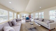 Located at Cobble Creek Circle in Rocklin, California, this community clubhouse offers a welcoming and well-appointed gathering space designed for comfort and socializing. The single-floor layout centers around a spacious living room that immediately impresses with its vaulted, cathedral-style ceiling, which lends a sense of openness and grandeur to the interior.

Natural light is a defining feature throughout, with an abundance of windows fitted with blinds lining multiple walls and allowing views of the surrounding greenery. Recessed lighting complements the natural light, ensuring the space remains bright and inviting at any time of day. The flooring is finished in neutral-toned ceramic tile, providing a clean and durable surface that runs throughout the main area.

The living room is furnished with generous seating arrangements, including plush gray sofas and accent chairs, centered around a glass-top coffee table and area rugs that define distinct lounge zones. A dining area with a round glass table and upholstered chairs provides a casual gathering spot, while a wall-mounted television and media console offer entertainment options.

French doors open directly to an outdoor pool area, seamlessly blending indoor comfort with outdoor leisure. A full-size refrigerator adds convenient amenity functionality. The warm, neutral color palette and thoughtful layout make this clubhouse a practical and pleasant community hub.