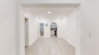 Located at 900 Pennsylvania Ave in Miami Beach, FL, this 1-bedroom, 1-bathroom unit offers a clean, modern aesthetic throughout its single-floor layout. The open living area is defined by crisp white walls and large-format light gray tile flooring that extends seamlessly through the space, creating a bright and airy atmosphere. Recessed lighting supplements the natural light that filters in through the windows.

The kitchen is accessed through a distinctive arched entryway and is outfitted with white shaker-style cabinetry, white quartz countertops, a granite tile backsplash, and stainless steel appliances including a gas range with an overhead ventilation hood. The design is both functional and visually cohesive.

The bedroom features a wall-mounted split A/C unit and large windows that offer views of the surrounding Miami Beach streetscape, including lush palm trees, allowing for generous natural light. The room is finished with the same tile flooring found throughout the unit.

The bathroom is neatly appointed with a white vanity topped with a quartz surface, brushed nickel hardware, and a decorative round mirror. A glass-enclosed shower completes the space. The unit also includes an intercom system near the entry door, adding a layer of convenience and security to this well-maintained Miami Beach residence.