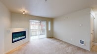 This single-floor, one-bedroom, one-bathroom unit offers a thoughtfully organized layout across a compact but efficient footprint. The living area serves as the heart of the unit, featuring soft wall-to-wall carpeting, a textured ceiling, and a built-in electric fireplace that adds warmth and visual interest. A large sliding glass door fitted with vertical blinds opens to an outdoor balcony, flooding the space with natural light and providing exterior views. A sidelight window adjacent to the sliding door enhances this brightness further.

The kitchen is well-appointed with warm wood cabinetry, dark granite-style countertops, hardwood flooring, and stainless steel appliances including a refrigerator and dishwasher. A pass-through counter adds functionality and a sense of openness between the kitchen and living areas.

The bedroom is a comfortable, carpeted room featuring a dedicated baseboard heater and a window overlooking the surrounding exterior. A walk-in closet with wire shelving provides practical storage. The bathroom includes a soaking tub with a shower surround and hardwood-style flooring. A hallway connects all rooms, contributing to a logical and convenient flow throughout the unit.