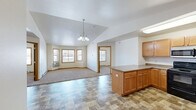 This single-floor, 2-bedroom, 2-bathroom residence in Minot, North Dakota offers a practical and comfortable layout designed for everyday living. The open-concept kitchen and dining area serves as the heart of the home, featuring warm honey-toned wood cabinetry, a central island with laminate countertops, and stainless steel appliances including a refrigerator and dishwasher. Stone-look vinyl tile flooring runs throughout the kitchen and dining space, while a vaulted ceiling adds a sense of openness and volume. A chandelier overhead enhances the living room, which flows naturally from the kitchen and is finished with plush carpeting. Multiple windows fitted with blinds allow natural light to fill the shared living areas. Both bedrooms are carpeted and well-proportioned, with the primary bedroom featuring multiple windows that bring in ample light. Each room benefits from baseboard heating. The two bathrooms include a full tub-shower combo with clean white tile surround. A dedicated in-unit laundry room accommodates a full-sized washer and dryer. Two closets provide additional storage throughout the home. The layout is efficient and thoughtfully organized, making this a highly functional residence in a residential Minot neighborhood.