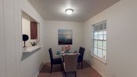 This single-story, one-bedroom, one-bathroom unit features a practical and efficient floor plan designed to maximize usable space. The living area is finished with wall-to-wall carpet and neutral white walls, creating a clean, versatile backdrop suitable for a variety of furnishing styles. A window allows natural light to filter in, brightening the room. The dining area is a defined space adjacent to the kitchen, featuring carpet flooring and a window with blinds that provides additional natural light. A pass-through window connects the dining area to the kitchen, enhancing the open feel between these spaces. The kitchen includes cabinetry with a warm wood finish and tile flooring, offering a functional layout for everyday cooking. The bedroom is a generously sized, carpeted room equipped with a ceiling fan with integrated lighting, ensuring year-round comfort. A window with blinds provides natural light, and direct access to the bathroom adds convenience. The bathroom features wood-style flooring, a tiled tub-shower combination with a curtain, a toilet, and a vanity with dark wood cabinetry, completing this straightforward and practical living space.