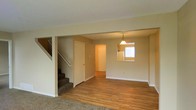This two-floor home offers a practical and welcoming layout designed for comfortable everyday living. The main level showcases warm hardwood flooring that extends throughout the open living and dining areas, creating a cohesive and inviting atmosphere. Neutral-toned walls complement the light hardwood, contributing to a bright and airy feel throughout the space.

A notable architectural feature on the main floor is the pass-through window connecting the kitchen to the dining area, allowing for easy interaction between the two spaces while maintaining a sense of defined zones. The kitchen, visible through the pass-through, benefits from natural light provided by a window, keeping the area well-lit. A pendant light fixture hangs above the dining area, adding a subtle decorative touch.

The staircase, finished with carpet, leads to the upper floor and is positioned alongside a closet door, offering convenient storage on the main level. The transition between the carpeted stair area and the hardwood living space clearly delineates the functional zones of the home. Overall, the space presents a clean, straightforward design with practical finishes suited for a variety of lifestyles.