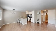 This well-appointed single-floor unit offers a clean, modern aesthetic defined by neutral warm-gray walls, crisp white trim, and wood-look flooring that flows consistently throughout the space. The open-concept layout connects the living area and kitchen, creating a seamless and functional living environment filled with natural light from multiple windows fitted with white blinds. The kitchen is a standout feature, anchored by a peninsula with a light quartz countertop, an undermount sink, and bar seating for casual dining. White shaker cabinetry reaches toward the ceiling, providing ample storage, while a full suite of stainless steel appliances — including a refrigerator, electric range, built-in microwave, and dishwasher — completes the space. A contemporary chandelier-style light fixture adds a decorative touch above the living and dining area. The bedrooms are generously proportioned, each with large windows that invite natural light. One bedroom features a ceiling fan and mirrored sliding closet doors. The bathroom is elegantly finished with large-format tile in the walk-in glass shower, a stone-topped vanity, and a backlit mirror, offering a spa-like atmosphere. Overall, the space presents a cohesive, move-in-ready environment with modern finishes throughout.