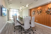 Located at 1801 Peachtree St NE in Atlanta's vibrant Buckhead corridor, this polished commercial suite delivers a sophisticated and functional environment designed for professional use. The space is unified by light wood-look flooring, neutral textured wall coverings, and clean white trim that lend a cohesive, contemporary aesthetic throughout.

The centerpiece is an elegantly appointed conference room accommodating a large party around a dark wood table paired with upholstered cream chairs. Artistic pendant lighting in varied glass forms cascades above the table, while floor-to-ceiling windows draped with sheer curtains invite abundant natural light and offer views of the Atlanta skyline. A wall-mounted display screen provides full AV capability for presentations and meetings.

A separate workspace corridor features built-in desk surfaces, warm wood accent wall panels, and curated sculptural artwork, creating an inspiring yet focused environment. Glass-paneled double doors connect areas seamlessly, allowing borrowed light to flow and maintaining an open, airy feel across the floor plate.

A dedicated kitchenette rounds out the suite, complete with white cabinetry, a white quartz countertop, an undermount sink, and a stainless steel beverage refrigerator — ideal for hosting clients or supporting daily team needs. Recessed and track lighting throughout ensures well-lit, comfortable conditions in every area.