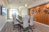 Located at 1801 Peachtree St NE in Atlanta's vibrant Buckhead corridor, this polished commercial suite delivers a sophisticated and functional environment designed for professional use. The space is unified by light wood-look flooring, neutral textured wall coverings, and clean white trim that lend a cohesive, contemporary aesthetic throughout.

The centerpiece is an elegantly appointed conference room accommodating a large party around a dark wood table paired with upholstered cream chairs. Artistic pendant lighting in varied glass forms cascades above the table, while floor-to-ceiling windows draped with sheer curtains invite abundant natural light and offer views of the Atlanta skyline. A wall-mounted display screen provides full AV capability for presentations and meetings.

A separate workspace corridor features built-in desk surfaces, warm wood accent wall panels, and curated sculptural artwork, creating an inspiring yet focused environment. Glass-paneled double doors connect areas seamlessly, allowing borrowed light to flow and maintaining an open, airy feel across the floor plate.

A dedicated kitchenette rounds out the suite, complete with white cabinetry, a white quartz countertop, an undermount sink, and a stainless steel beverage refrigerator — ideal for hosting clients or supporting daily team needs. Recessed and track lighting throughout ensures well-lit, comfortable conditions in every area.