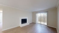 Located at 2400 Briarwest Blvd in Houston, Texas, this well-appointed two-bedroom, one-bathroom home is thoughtfully laid out across a single floor. The living room serves as the heart of the home, featuring light wood flooring, crown molding, and a classic fireplace as a focal point. A full-width sliding glass door fills the room with natural light and provides direct access to a private patio with outdoor views. The galley-style kitchen is efficiently designed with grey cabinetry, granite-look countertops, black appliances including a range and refrigerator, a stainless steel sink, and a dishwasher. A pass-through opening connects the kitchen to the living area, enhancing the open feel. A pendant light fixture illuminates the transitional hallway between rooms. The spacious primary bedroom features plush carpeting, crown molding, a ceiling fan with light, and a window overlooking the outdoors. It offers convenient access to the shared bathroom, which is finished with a vanity featuring grey cabinetry and a tub-shower combination with white tile surround. The second bedroom is similarly carpeted with crown molding. Wood-look flooring runs throughout the main living areas and hallways, creating a cohesive, clean aesthetic throughout the home.