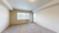 This 2-bedroom, 1-bathroom unit at 12928 E Mansfield Ave in Spokane Valley, WA offers a practical, single-floor layout designed to maximize its compact footprint. The living room serves as the central gathering space, featuring wall-to-wall carpeting in a neutral tone, a large multi-pane window that invites ample natural light, and a glass-panel exterior door providing outdoor access. A wall-unit HVAC system ensures year-round climate control.

The kitchen is efficiently arranged with warm oak cabinetry, white laminate countertops, and a full suite of black appliances including a refrigerator, electric range, and built-in microwave. A double-basin sink sits along the peninsula counter, and tile-style flooring ties the space together. An adjacent hallway connects to an in-unit laundry area.

The primary bedroom offers carpeted flooring and a window with exterior views, while the second bedroom mirrors this layout with its own closet and natural light. The bathroom features an oak vanity with a large mirror, a shower/tub combination, a baseboard heater, and tile-style flooring, completing this straightforward and functional unit.