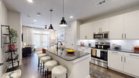 This thoughtfully designed one-bedroom, one-bathroom residence offers a smart, efficient layout across a single floor. The open-concept kitchen anchors the living space with crisp white cabinetry, dark granite countertops, a classic subway tile backsplash, and a full suite of stainless steel appliances. A central kitchen island with a waterfall granite countertop and seating for multiple bar stools serves as both a functional workspace and social hub, illuminated by a pair of striking black pendant lights overhead. Hardwood-style flooring runs throughout the main living areas, lending warmth and continuity to the space. The living room is bright and inviting, benefiting from natural light streaming through large windows and a set of French doors that open to the outdoors, complemented by a ceiling fan above. The bedroom is a comfortable retreat, featuring plush carpeting, ample natural light from oversized windows, and direct access to the bathroom. The bathroom is finished with a granite-topped vanity, a backlit mirror, and a walk-in closet with built-in shelving, providing generous storage. Clean lines, neutral tones, and modern black hardware finishes throughout give this residence a cohesive, contemporary aesthetic.