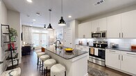 This thoughtfully designed one-bedroom, one-bathroom residence offers a smart, efficient layout across a single floor. The open-concept kitchen anchors the living space with crisp white cabinetry, dark granite countertops, a classic subway tile backsplash, and a full suite of stainless steel appliances. A central kitchen island with a waterfall granite countertop and seating for multiple bar stools serves as both a functional workspace and social hub, illuminated by a pair of striking black pendant lights overhead. Hardwood-style flooring runs throughout the main living areas, lending warmth and continuity to the space. The living room is bright and inviting, benefiting from natural light streaming through large windows and a set of French doors that open to the outdoors, complemented by a ceiling fan above. The bedroom is a comfortable retreat, featuring plush carpeting, ample natural light from oversized windows, and direct access to the bathroom. The bathroom is finished with a granite-topped vanity, a backlit mirror, and a walk-in closet with built-in shelving, providing generous storage. Clean lines, neutral tones, and modern black hardware finishes throughout give this residence a cohesive, contemporary aesthetic.