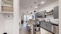 Located at 2351 Plaza Blvd in Richardson, TX, this thoughtfully designed one-bedroom, one-bathroom residence offers a modern aesthetic throughout its efficiently organized single-floor layout. The open-concept living and kitchen area serves as the heart of the unit, where light wood-style flooring, white walls, and recessed lighting create a bright, contemporary atmosphere.

The kitchen is well-appointed with gray shaker-style cabinetry, dark countertops, a white subway tile backsplash, and a full suite of stainless steel appliances, including a French door refrigerator, microwave, and range. A central island with pendant lighting overhead provides additional workspace and casual seating. Built-in open shelving adds a functional decorative element near the entrance.

The living room features French doors that open to a private balcony, allowing natural light to fill the space. The bedroom is a comfortable, carpeted retreat with a large window, while the bathroom offers a dark-countered vanity with ample storage, a large mirror, and a glass-enclosed walk-in shower. A dedicated laundry area houses a stacked washer and dryer unit, completing this well-equipped residence.