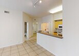 Located at 12325 SW 151st Street in Miami, FL, this single-floor unit offers a functional and well-organized layout. The entryway welcomes you with light tile flooring, a flush ceiling fixture, and a conveniently located electrical panel. From here, the space opens into a combined living and dining area finished in the same neutral tile, creating a cohesive flow throughout the common areas.

The kitchen features warm wood-toned cabinetry, dark countertops, a breakfast bar peninsula, and built-in track lighting overhead. White appliances including a range, microwave, and refrigerator are integrated into the cabinetry. The kitchen connects seamlessly to the living area, making the space feel open and accessible.

The bedroom is finished with light hardwood-style flooring and benefits from a large window with views of lush tropical greenery, allowing natural light to fill the room. A sliding glass door in a secondary area opens to an outdoor space framed by palm foliage, adding a refreshing connection to the outdoors.

The bathroom is well-appointed with a tile-surround glass-enclosed shower, a single vanity with a wide mirror, and tile flooring. A utility area connects the bathroom to the bedroom, offering additional functionality. Overall, the unit presents a clean, neutral palette with practical finishes throughout.