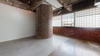 Located in Washington, DC's vibrant New York Avenue corridor, Unit 602 at 1401 New York Ave NE is a single-floor loft that masterfully preserves the raw character of its industrial origins while incorporating modern finishes. The main living area is immediately commanding, anchored by a dramatic cylindrical brick column that rises to exposed concrete ceiling beams overhead. A row of large factory-style windows lines one wall, flooding the space with generous natural light and lending an open, airy atmosphere. Polished concrete floors extend throughout, complementing the exposed structural elements, while ceiling fans and strung accent lighting add warmth to the industrial aesthetic.

The kitchen is efficiently designed with rich, dark-stained cabinetry offering ample storage, light countertops, and a full suite of stainless steel appliances including a refrigerator, electric range, over-the-range microwave, and dishwasher. The clean contrast between the cabinetry and appliances gives the kitchen a polished, contemporary feel.

The bathroom continues the design's attention to detail, featuring classic black-and-white penny tile flooring, subway-tiled shower walls, a white vanity with dark countertop, and clean, bright walls that contribute to a timeless, refined finish.