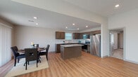 This single-story residence offers a thoughtfully designed open-concept layout that seamlessly connects the kitchen, dining, and living areas. The kitchen is a standout feature, showcasing rich dark-stained cabinetry, granite-look countertops, a subway tile backsplash, a central island with additional counter space, and a full suite of stainless steel appliances including a range, over-the-range microwave, dishwasher, and refrigerator. Light wood-look flooring runs throughout the main living areas, lending warmth and continuity to the space.

The dining area benefits from a large sliding glass door that frames views of the surrounding greenery, filling the room with natural light. The primary bedroom is a refined retreat, distinguished by an elegant tray ceiling, a ceiling fan, plush carpet, and access to a walk-in closet as well as an en-suite bathroom. Additional bedrooms are carpeted and equipped with ceiling fans and windows that invite natural light. The bathroom features wood-look flooring, a granite-top vanity with dark cabinetry, and a tub-shower combination. Recessed lighting is present throughout, contributing to a clean, modern ambiance across all areas of the home.