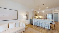 Located at 3542 Aspire Cir in Cape Coral, Florida, this single-floor residence offers a clean, contemporary aesthetic defined by crisp white walls, light wood flooring, and an abundance of natural light throughout. The open-concept living and kitchen area serves as the heart of the home, where a well-appointed kitchen features shaker-style cabinetry in a soft neutral tone, stainless steel appliances including a refrigerator, range, microwave, and dishwasher, and a large peninsula with bar seating illuminated by stylish pendant lighting. The kitchen flows seamlessly into the living area, which is bright and welcoming, with a coastal-inspired palette and access to outdoor views through sliding glass doors. A hallway connects the main living space to the private areas of the home, including a tranquil bedroom bathed in soft natural light from large windows dressed with sheer curtains and blinds. The bedroom is generously proportioned, offering a calm retreat with warm, neutral tones. The bathroom is finished with a dual-sink vanity topped in white, floor-to-ceiling cabinetry, a large mirror with bright vanity lighting, and hardwood-style flooring. Throughout the residence, the design maintains a cohesive, airy ambiance that reflects the relaxed elegance of Southwest Florida living.