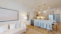Located at 3542 Aspire Cir in Cape Coral, Florida, this single-floor residence offers a clean, contemporary aesthetic defined by crisp white walls, light wood flooring, and an abundance of natural light throughout. The open-concept living and kitchen area serves as the heart of the home, where a well-appointed kitchen features shaker-style cabinetry in a soft neutral tone, stainless steel appliances including a refrigerator, range, microwave, and dishwasher, and a large peninsula with bar seating illuminated by stylish pendant lighting. The kitchen flows seamlessly into the living area, which is bright and welcoming, with a coastal-inspired palette and access to outdoor views through sliding glass doors. A hallway connects the main living space to the private areas of the home, including a tranquil bedroom bathed in soft natural light from large windows dressed with sheer curtains and blinds. The bedroom is generously proportioned, offering a calm retreat with warm, neutral tones. The bathroom is finished with a dual-sink vanity topped in white, floor-to-ceiling cabinetry, a large mirror with bright vanity lighting, and hardwood-style flooring. Throughout the residence, the design maintains a cohesive, airy ambiance that reflects the relaxed elegance of Southwest Florida living.