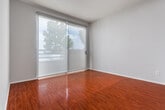 Located at 165 N Hoover St in the heart of Los Angeles, CA, this single-floor unit offers a well-appointed, functional layout with consistent design elements throughout. The kitchen is a standout feature, showcasing white shaker-style cabinetry that extends to the ceiling for ample storage, granite-style countertops, and a full suite of stainless steel appliances including a gas range, dishwasher, and refrigerator. Track lighting and an under-cabinet range hood add practical illumination to the space. Rich, warm hardwood-style flooring flows seamlessly throughout the unit, lending continuity and warmth to every room. The living and bedroom areas are finished with neutral gray walls that complement the flooring, and large windows — including a set of expansive sliding glass doors fitted with sheer roller shades — invite abundant natural light and outdoor views. The bedroom benefits from a dedicated window framing neighborhood scenery. The bathroom is cleanly finished with light tile flooring, a white vanity with granite-style countertop, a large mirror, and a shower-tub combo with glass sliding doors. Overall, the unit presents a clean, modern aesthetic well-suited to comfortable urban living in Los Angeles.
