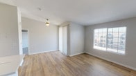 This single-floor residence offers a clean, modern aesthetic with a thoughtfully designed layout visible throughout. The open living area is finished with light wood-look flooring that extends seamlessly into the kitchen, creating a cohesive and airy feel. Large windows fitted with blinds invite natural light into the space, offering views of the surrounding neighborhood.

The kitchen is well-appointed with crisp white cabinetry, a stainless steel refrigerator, an electric range, a peninsula with a sink and light countertops, and track lighting overhead — making it both functional and visually appealing. It opens directly to the living area, reinforcing the open-concept flow.

The bedroom features soft, plush carpeting, a generous window for natural light, and a textured ceiling, providing a comfortable and quiet retreat. A closet with vertical blinds adds practical storage.

The bathroom is finished with wood-look flooring, a white tiled tub-shower combo, a toilet, and a vanity with a light countertop, maintaining the clean and neutral palette found throughout the unit.

A dedicated in-unit laundry area houses a full-sized top-load washer and dryer side by side, with overhead wire shelving for added storage convenience. Throughout, neutral gray walls and white trim create a fresh, move-in-ready atmosphere.