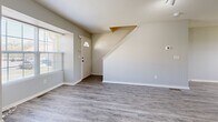 This three-story townhome in Kansas City, MO offers a well-organized layout across three distinct levels, providing ample space for comfortable living. The main floor features a combined kitchen and living area, where gray-toned hardwood-style flooring flows seamlessly throughout. The living room is bright and open, with natural light streaming through large windows and a staircase anchoring the space. The kitchen is well-appointed with light wood cabinetry, stainless steel appliances including a range, microwave, dishwasher, and refrigerator, along with a peninsula counter that adds both prep space and a casual dining option. A pendant chandelier accents the dining area, which benefits from generous window light. Each of the three bedrooms is carpeted for comfort and equipped with a ceiling fan. The generously sized primary bedroom includes a walk-in closet. Additional bedrooms feature natural light from windows and ample closet access. Three full bathrooms are distributed across the floors, each with a tub-shower combination and tile flooring in a classic hexagonal pattern. A dedicated utility room and two additional closets provide practical storage. The multi-level design, connected by two staircases, offers a functional and private living experience throughout.