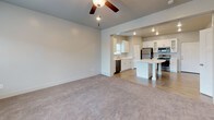 This two-story home offers a thoughtfully laid-out interior with a clean, contemporary aesthetic throughout. The main level centers around an open-plan living and kitchen area, where plush carpeting in the living room transitions to durable wood-look flooring in the kitchen. A ceiling fan with recessed lighting illuminates the spacious living area, which receives natural light through a large window overlooking the neighborhood. The front entry door opens directly into this welcoming space, with a staircase providing access to the upper level.

The kitchen is well-appointed with white shaker-style cabinetry, light quartz countertops, a double-basin sink, and a full suite of stainless steel appliances, including a refrigerator, electric range, microwave, and dishwasher. A central island adds additional counter space and functionality.

Upstairs, multiple carpeted bedrooms feature neutral walls and blinds-fitted windows that bring in natural light and neighborhood views. The primary suite connects to a bathroom with a long white vanity, ample cabinet storage, and a walk-in closet with built-in shelving. A secondary bathroom serves the remaining bedrooms, complete with a white vanity with dark countertop, a mirror, and a tub-shower combination.