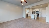 This two-story home offers a thoughtfully laid-out interior with a clean, contemporary aesthetic throughout. The main level centers around an open-plan living and kitchen area, where plush carpeting in the living room transitions to durable wood-look flooring in the kitchen. A ceiling fan with recessed lighting illuminates the spacious living area, which receives natural light through a large window overlooking the neighborhood. The front entry door opens directly into this welcoming space, with a staircase providing access to the upper level.

The kitchen is well-appointed with white shaker-style cabinetry, light quartz countertops, a double-basin sink, and a full suite of stainless steel appliances, including a refrigerator, electric range, microwave, and dishwasher. A central island adds additional counter space and functionality.

Upstairs, multiple carpeted bedrooms feature neutral walls and blinds-fitted windows that bring in natural light and neighborhood views. The primary suite connects to a bathroom with a long white vanity, ample cabinet storage, and a walk-in closet with built-in shelving. A secondary bathroom serves the remaining bedrooms, complete with a white vanity with dark countertop, a mirror, and a tub-shower combination.