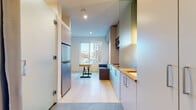 This single-floor unit exemplifies smart, modern design with a highly efficient layout that maximizes every inch of available space. The entryway features large-format tile flooring that transitions seamlessly into the kitchen area, where light gray cabinetry — both upper and lower — pairs with warm butcher-block countertops for a contemporary yet inviting aesthetic. A stainless steel refrigerator, built-in microwave, and a compact sink complete the functional kitchen setup.

The living area flows naturally from the kitchen and is anchored by light hardwood flooring that brightens the overall atmosphere. A large window at the far end of the room frames views of the surrounding urban landscape, flooding the space with natural light. A multi-functional wooden table with a metal base and a gray upholstered sofa define the living zone, while a ceiling-mounted air conditioning unit ensures year-round comfort.

A built-in storage wall unit with open shelving and cabinets provides ample organization, and a Murphy bed system offers flexible sleeping arrangements without compromising the open feel of the main living area. A gray curtain partition provides privacy between zones. The bathroom is clean and minimalist, featuring tile flooring, a toilet with grab bar support, and a curtained entry, maintaining the unit's cohesive, functional design throughout.