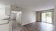 Located at 415 NE Delaware Ave in Ankeny, Iowa, this 2-bedroom, 1-bathroom unit offers a clean, modern aesthetic throughout its single-floor layout. Consistent light-toned vinyl plank flooring runs throughout the entire space, complementing the neutral beige walls and white trim found in every room.

The combined kitchen and living area forms the heart of the unit. The kitchen is well-appointed with white cabinetry, granite-style countertops, black appliances including a range, over-the-range microwave, dishwasher, and refrigerator, plus a ceiling-mounted track light. A peninsula provides additional counter space. The living area is bright and open, featuring a sliding glass door that leads to an outdoor patio and allows generous natural light to fill the room.

The primary bedroom offers a comfortable footprint with a double sliding-door closet and a window with outdoor views. The second bedroom is similarly finished with a window and a standard closet, maintaining the same neutral palette. A hallway connects the private areas of the unit.

The bathroom features a white vanity with a granite-topped sink, a full tub-shower combination, and matching vinyl flooring. Textured ceilings are present throughout, adding subtle architectural character to the otherwise clean, modern interior.