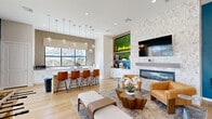 Located in Arlington, Texas, this single-floor community space is thoughtfully designed to serve as a welcoming and versatile gathering hub. The open-concept layout seamlessly connects a fully equipped kitchenette and multiple living and lounge areas, all finished with warm light wood flooring that flows throughout.

The kitchenette features crisp white cabinetry, ample countertop space, a built-in beverage refrigerator, and large black-framed windows that flood the area with natural light and offer views of the surrounding neighborhood. Adjacent lounge areas are anchored by a striking floor-to-ceiling stone fireplace with a mounted TV, complemented by bold teal accent walls that add a vibrant, modern contrast to the neutral palette.

The main living area is bright and spacious, with sliding glass doors that open directly to a covered outdoor patio. The patio, finished with light speckled flooring, is framed by black iron railings and offers scenic views of the community pool and landscaped grounds — ideal for relaxed outdoor seating and social gatherings. Inside, a shiplap-clad lounge nook and a foosball table add a playful, recreational dimension to the space.

Throughout, large-format windows maximize sunlight, while the cohesive blend of contemporary furnishings and architectural detail creates an inviting and functional community environment.
