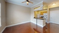 This single-floor space showcases a cohesive design highlighted by richly polished, deep-toned concrete floors that run throughout, lending a sleek and durable character to every room. Crown molding accents the ceilings, adding a refined architectural touch that complements the warm, neutral-toned walls.

The living area is bright and open, benefiting from multiple windows dressed with horizontal blinds that allow natural light to filter in. A ceiling fan with a light fixture provides both comfort and illumination, while a glass-paneled door opens to an exterior view, enhancing the sense of connectivity to the outdoors.

The kitchen is thoughtfully laid out in a galley style, featuring light wood cabinetry, dark granite countertops, a stainless steel sink, and white appliances including a refrigerator, electric range, and microwave. A peninsula with a granite countertop and bar seating bridges the kitchen and living area, creating a natural gathering point and reinforcing the open-concept flow.

The bathroom continues the granite countertop theme, with a wood-toned vanity, a tall storage cabinet, a large mirror, and a closet nearby, offering ample storage. A louvered closet panel near the entryway adds additional practical storage to this well-appointed space.
