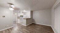 This single-floor, one-bedroom, one-bathroom unit offers a practical and well-organized layout designed to maximize every square foot of its compact footprint. Consistent wood-look laminate flooring flows throughout the living areas and bedroom, providing a warm and cohesive aesthetic that complements the neutral gray wall tones and crisp white baseboards found throughout.

The living room is a bright, open space featuring a ceiling fan with light fixture, a front entry door, and a window fitted with horizontal blinds that allow for natural light control. The room's clean lines and understated palette create a versatile canvas ready for personalization.

The kitchen area is visible in the floorplan view and includes light-colored countertops with a pass-through or breakfast bar element, along with white cabinetry, making efficient use of the available space.

The bedroom is a well-proportioned private retreat, also finished with wood-look flooring and neutral walls. It features a ceiling fan with lighting, a window with blinds for natural light, and a six-panel door that leads conveniently to the bathroom.

The bathroom is finished with beige ceramic tile surround in the tub/shower combination, complemented by tile flooring, and includes a standard toilet and full-size soaking tub, offering a clean and functional space. Overall, the unit presents a move-in ready, low-maintenance living environment.