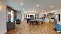 Located at 3125 Fire Ct in Charlotte, NC, this thoughtfully designed single-floor amenity space offers a seamless blend of modern aesthetics and functional communal living. Warm hardwood-style flooring flows continuously throughout, unifying the various activity zones within the open layout.

The lounge area anchors one end of the space, highlighted by a sleek built-in fireplace set within a richly paneled wood accent wall flanked by integrated shelving. A statement mid-century modern chandelier with brass accents adds a sophisticated glow, while large windows invite natural light and outdoor views.

The central gathering area features a billiards table and a generously sized dining table beneath an elegant multi-globe pendant light fixture, making it well-suited for both casual recreation and group events.

The kitchen area is a standout, appointed with white cabinetry, a striking natural stone backsplash, stainless steel appliances, and a waterfall-edge marble-look island with bar seating illuminated by gold-accented pendant lights.

A secondary lounge area offers a large sectional sofa, sculptural coffee tables, a wall-mounted display screen, and a bold drum chandelier, with French doors providing views of an outdoor pool area. Textured accent walls and curated décor details complete the refined, contemporary ambiance throughout.