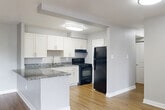 This thoughtfully designed one-bedroom, one-bathroom residence in District Heights, Maryland offers a clean, modern aesthetic across a single level of comfortable living space. The open-concept kitchen and living area serves as the heart of the home, where warm hardwood-style flooring flows throughout. The kitchen is well-equipped with crisp white shaker cabinets, granite countertops, a stainless steel sink, and black appliances including a gas range, dishwasher, and refrigerator. The living room is bright and inviting, highlighted by sliding glass doors that open onto a private balcony, filling the space with natural light and providing pleasant outdoor views. The generously sized bedroom features plush carpeting, a large window with blinds for natural light, and direct access to a spacious walk-in closet outfitted with dual hanging rods and shelving. The full bathroom showcases elegant marble-style tile surrounding the soaking tub and shower combination, complemented by a granite vanity countertop and dark cabinetry. Neutral gray walls, white trim, and consistent flooring choices tie the entire residence together, creating a cohesive and move-in-ready living environment.